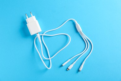 Photo of USB power adapter with triple charge cable on light blue background, top view