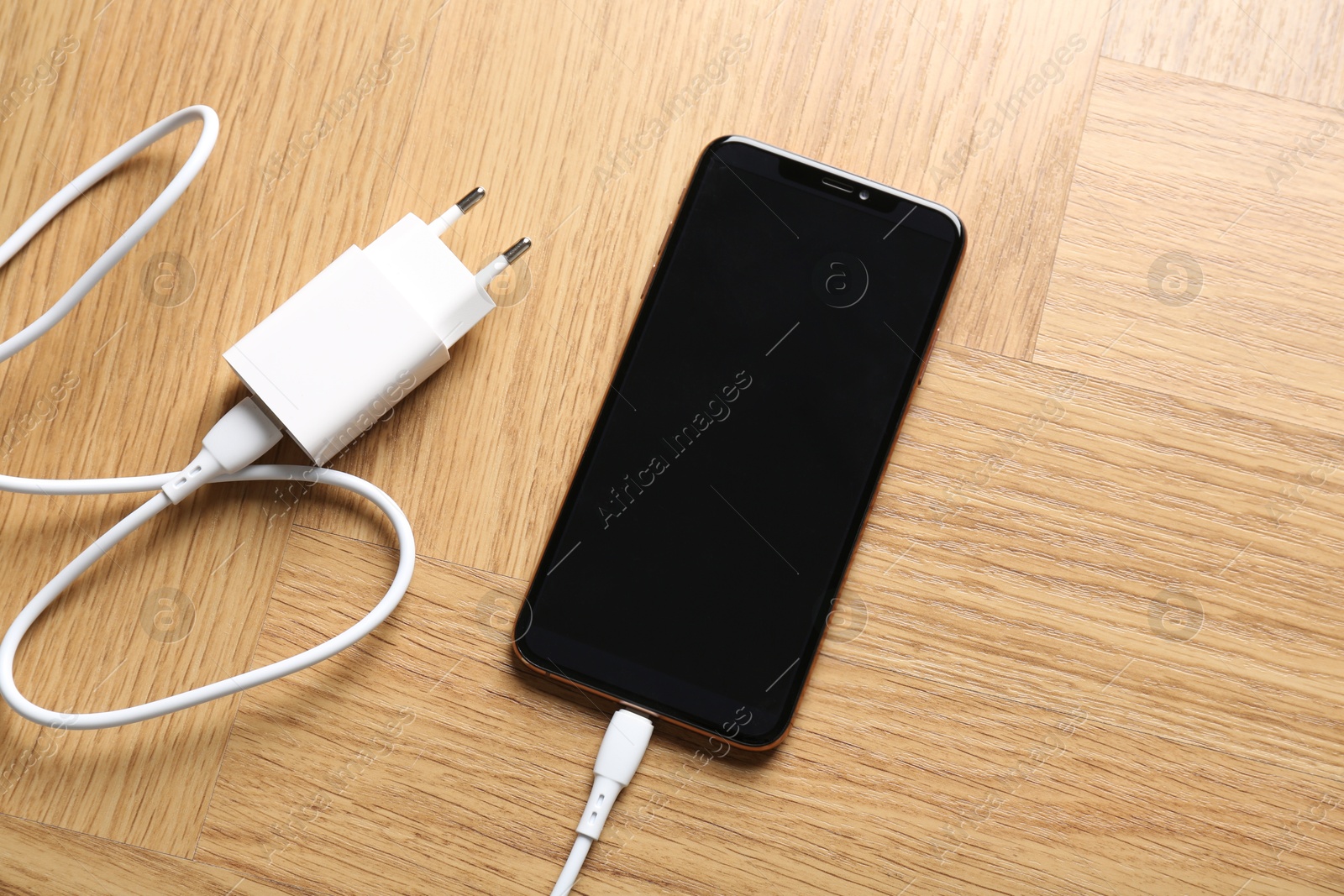 Photo of USB power adapter with charge cable connected to smartphone on wooden table, top view