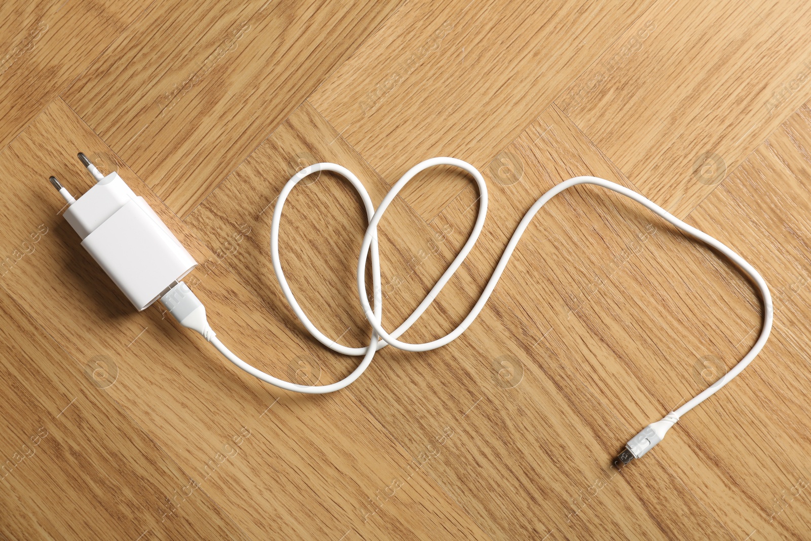 Photo of USB power adapter with charge cable on wooden table, top view