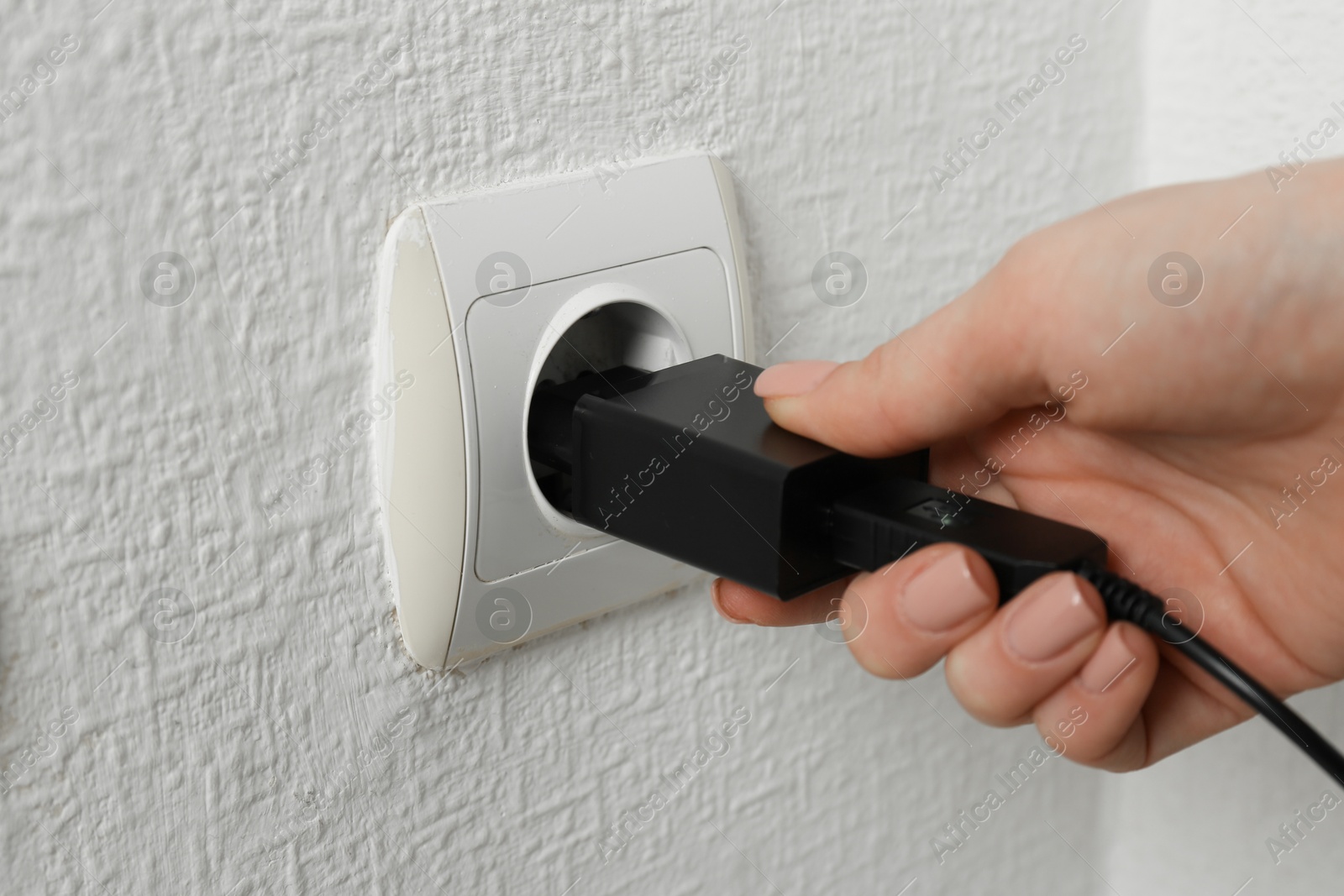 Photo of Woman plugging USB power adapter with charge cable into electrical socket indoors, closeup