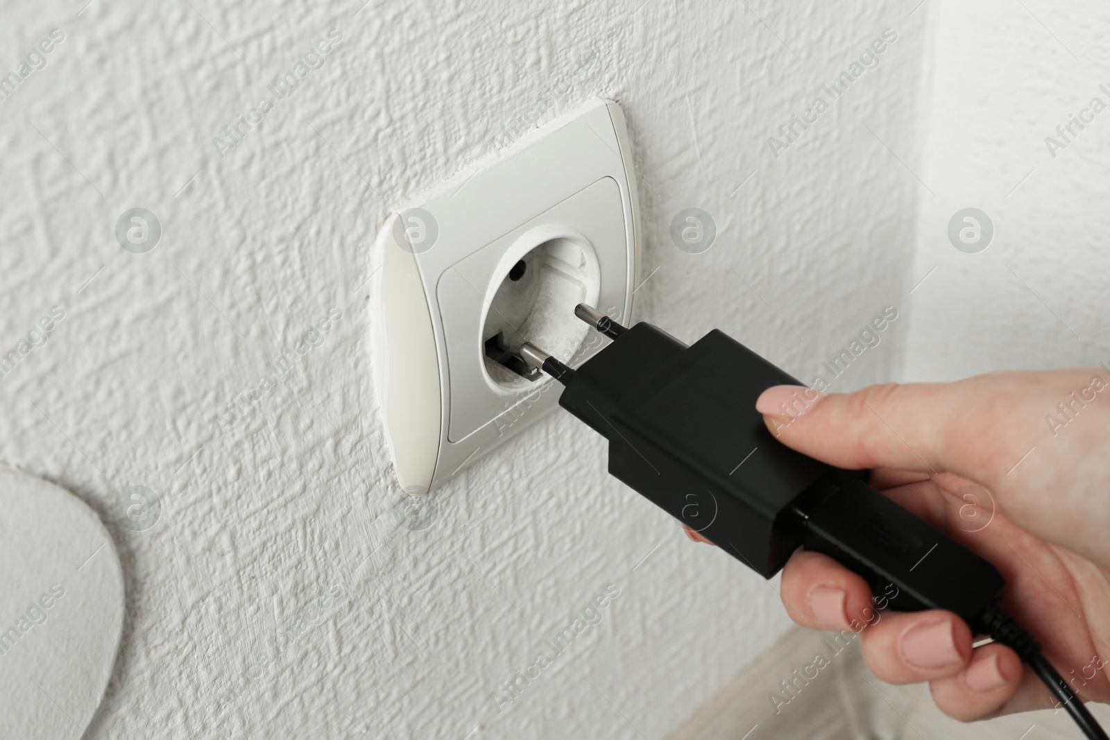 Photo of Woman plugging USB power adapter with charge cable into electrical socket indoors, closeup