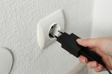 Photo of Woman plugging USB power adapter with charge cable into electrical socket indoors, closeup