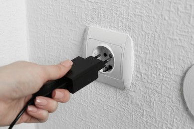 Photo of Woman plugging USB power adapter with charge cable into electrical socket indoors, closeup