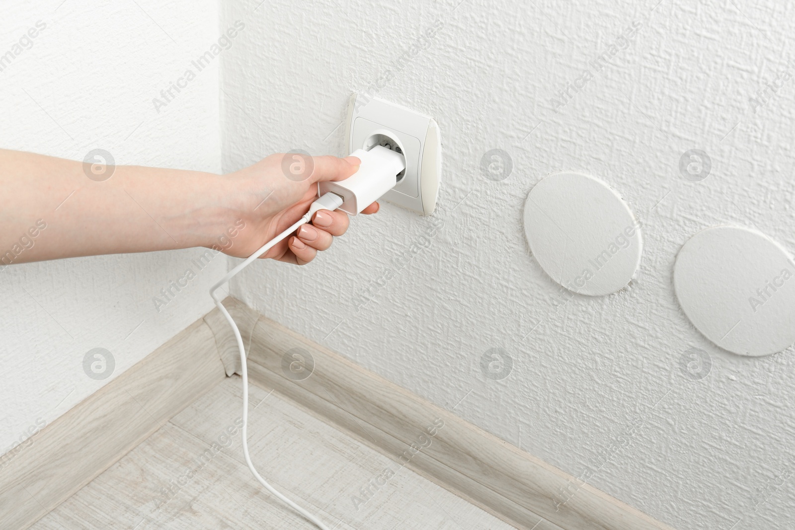 Photo of Woman plugging USB power adapter with charge cable into electrical socket indoors, closeup