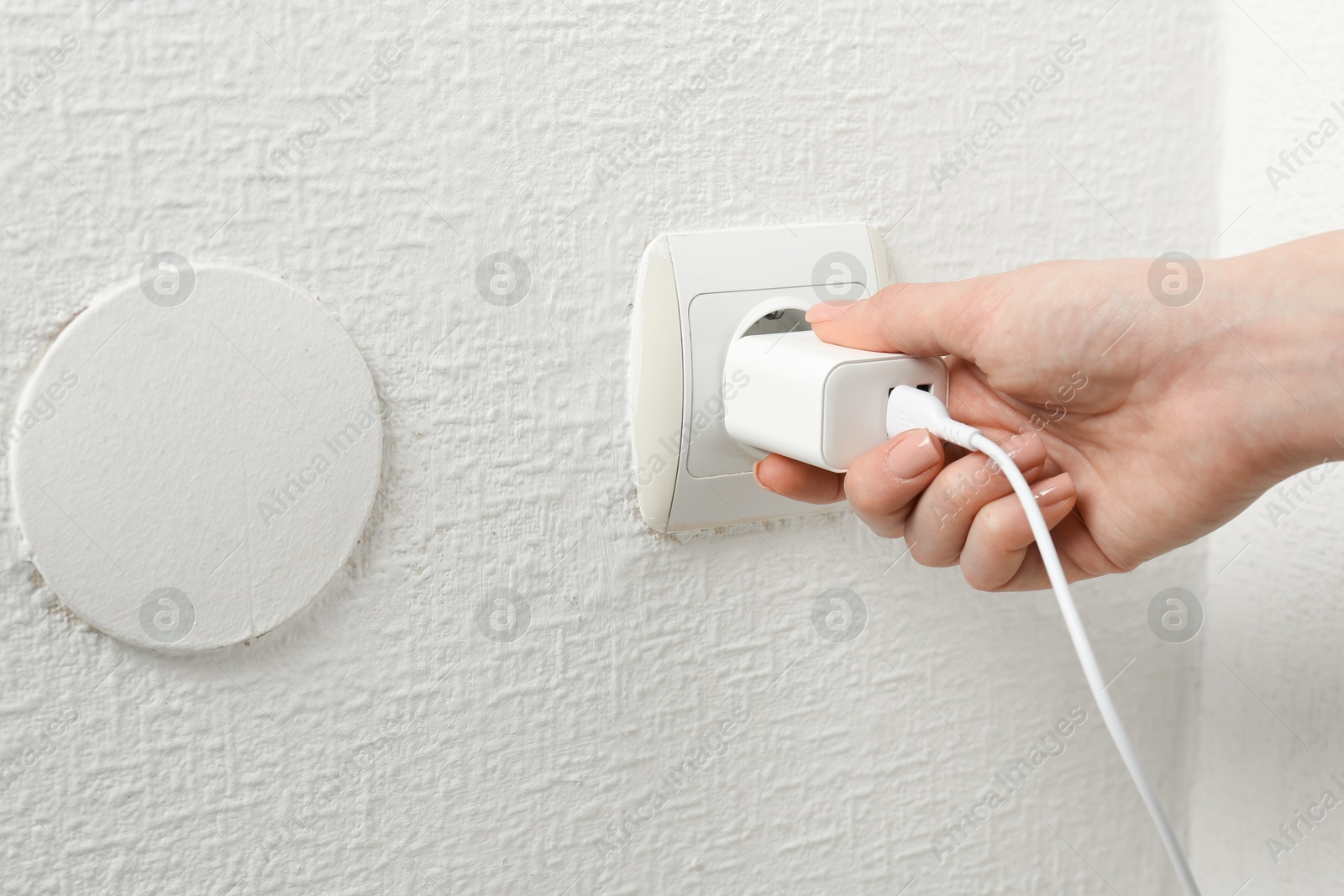 Photo of Woman plugging USB power adapter with charge cable into electrical socket indoors, closeup