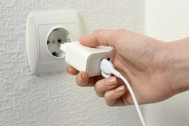 Photo of Woman plugging USB power adapter with charge cable into electrical socket indoors, closeup