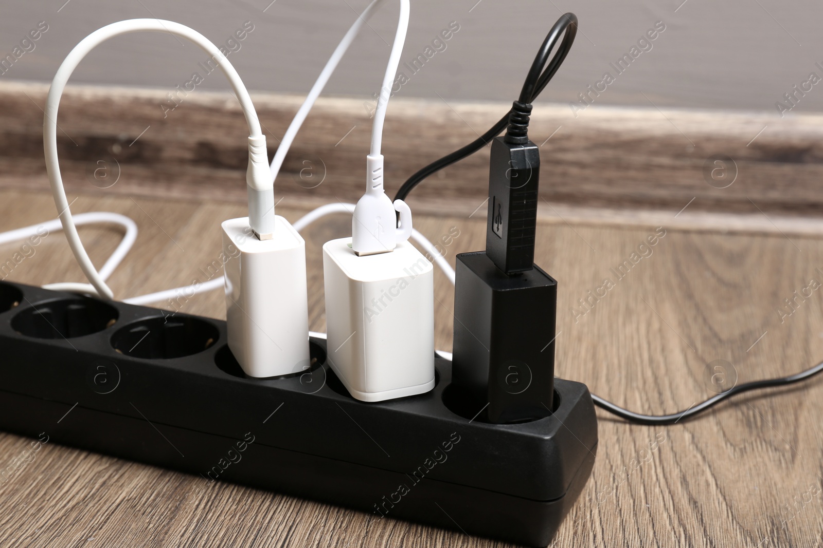 Photo of USB adapters with charge cables in power strip on floor indoors, closeup