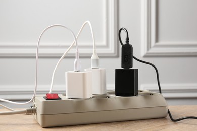 Photo of USB adapters with charge cables in power strip on wooden table indoors, closeup