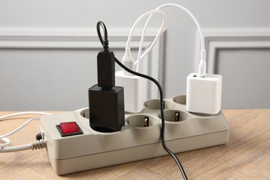 Photo of USB adapters with charge cables in power strip on wooden table indoors, closeup