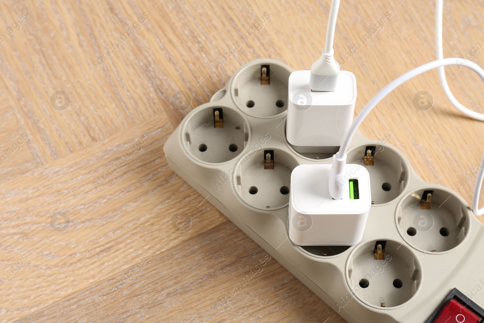 Photo of USB adapters with charge cables in power strip on wooden table, above view. Space for text