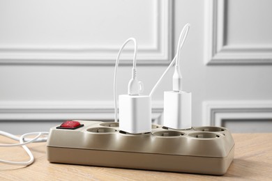 Photo of USB adapters with charge cables in power strip on wooden table indoors, closeup