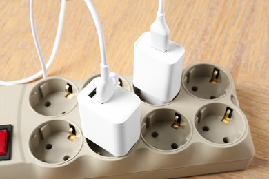 Photo of USB adapters with charge cables in power strip on wooden table, closeup