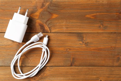 Photo of USB power adapter with charge cable on wooden table, top view. Space for text