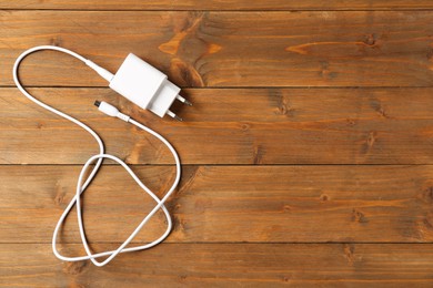 Photo of USB power adapter with charge cable on wooden table, top view. Space for text