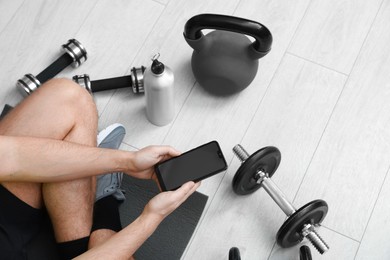 Photo of Man with smartphone and gym equipment on floor indoors, above view