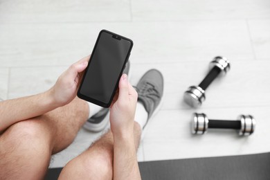 Photo of Man with smartphone and dumbbells on floor indoors, above view