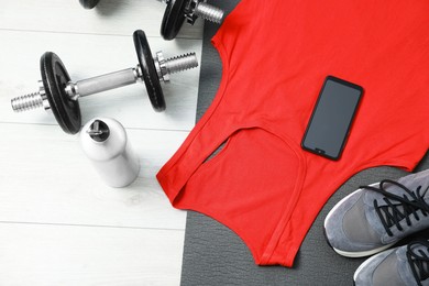 Photo of Sports tank top, smartphone and gym equipment on floor, flat lay