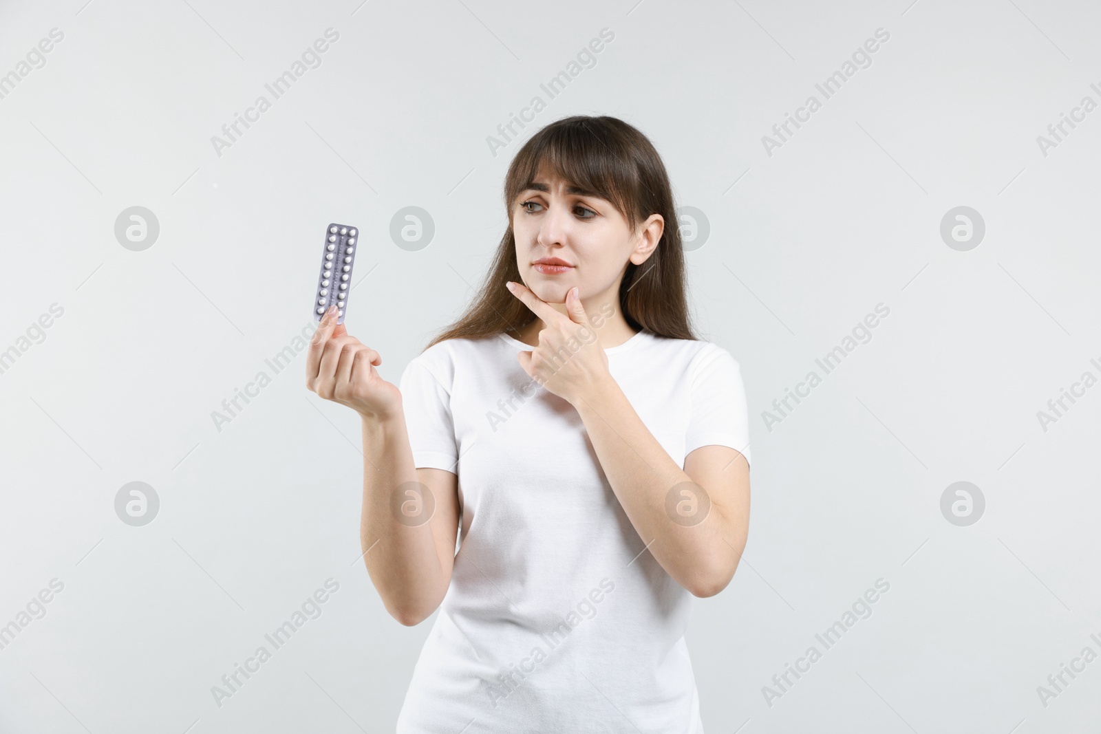 Photo of Pensive young woman with blister of contraceptive pills on light background