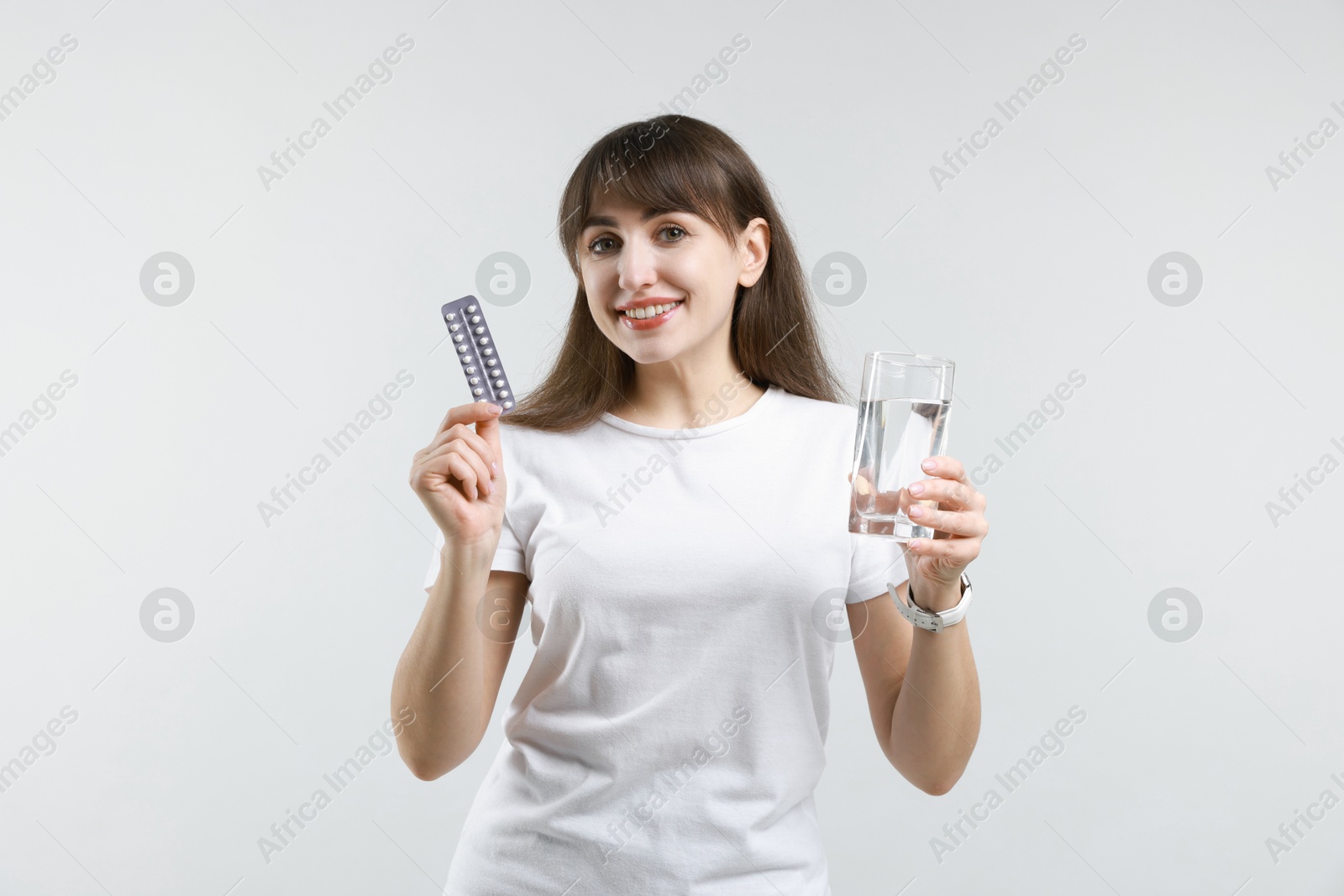 Photo of Smiling woman with contraceptive pills and glass of water on light background