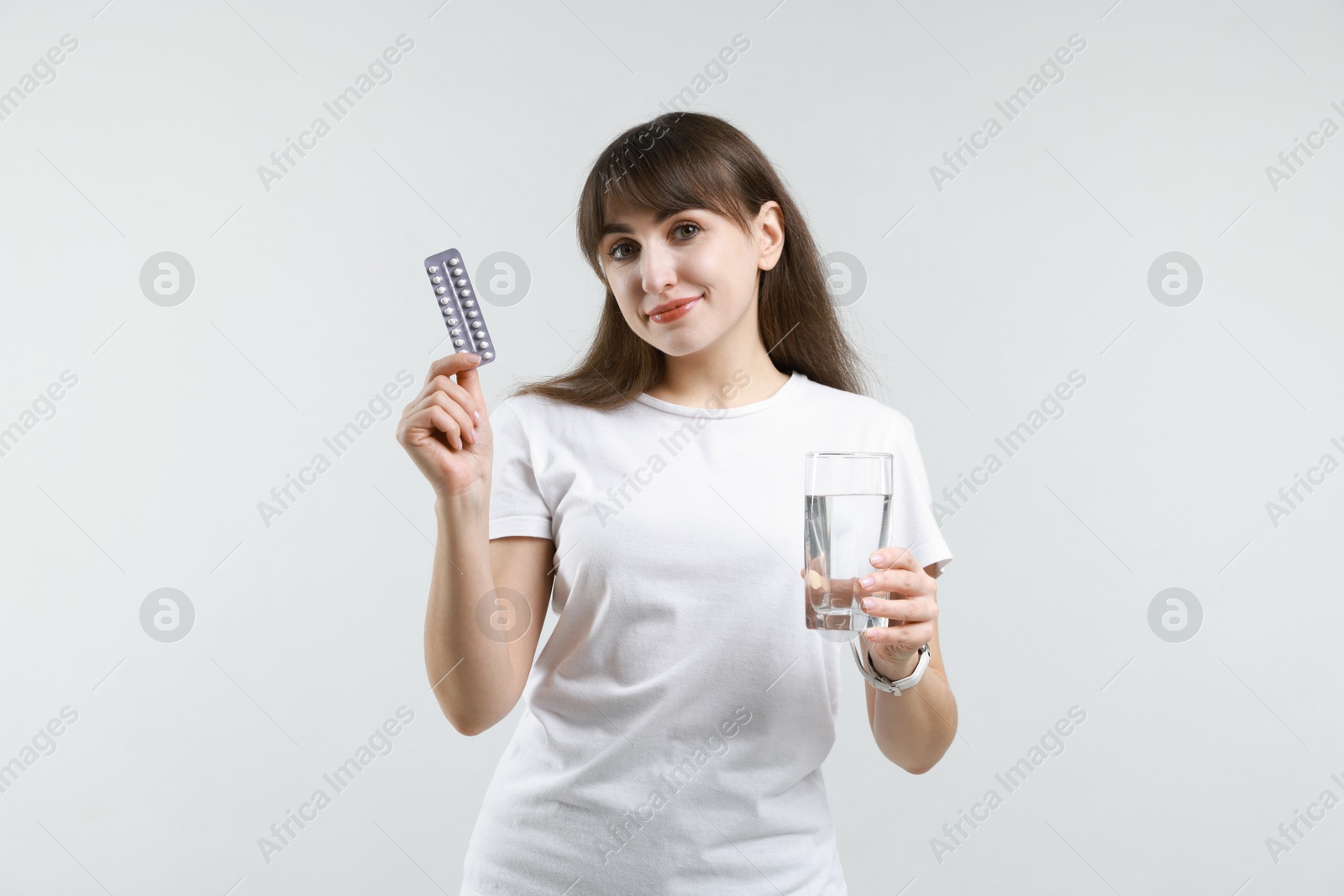 Photo of Smiling woman with contraceptive pills and glass of water on light background