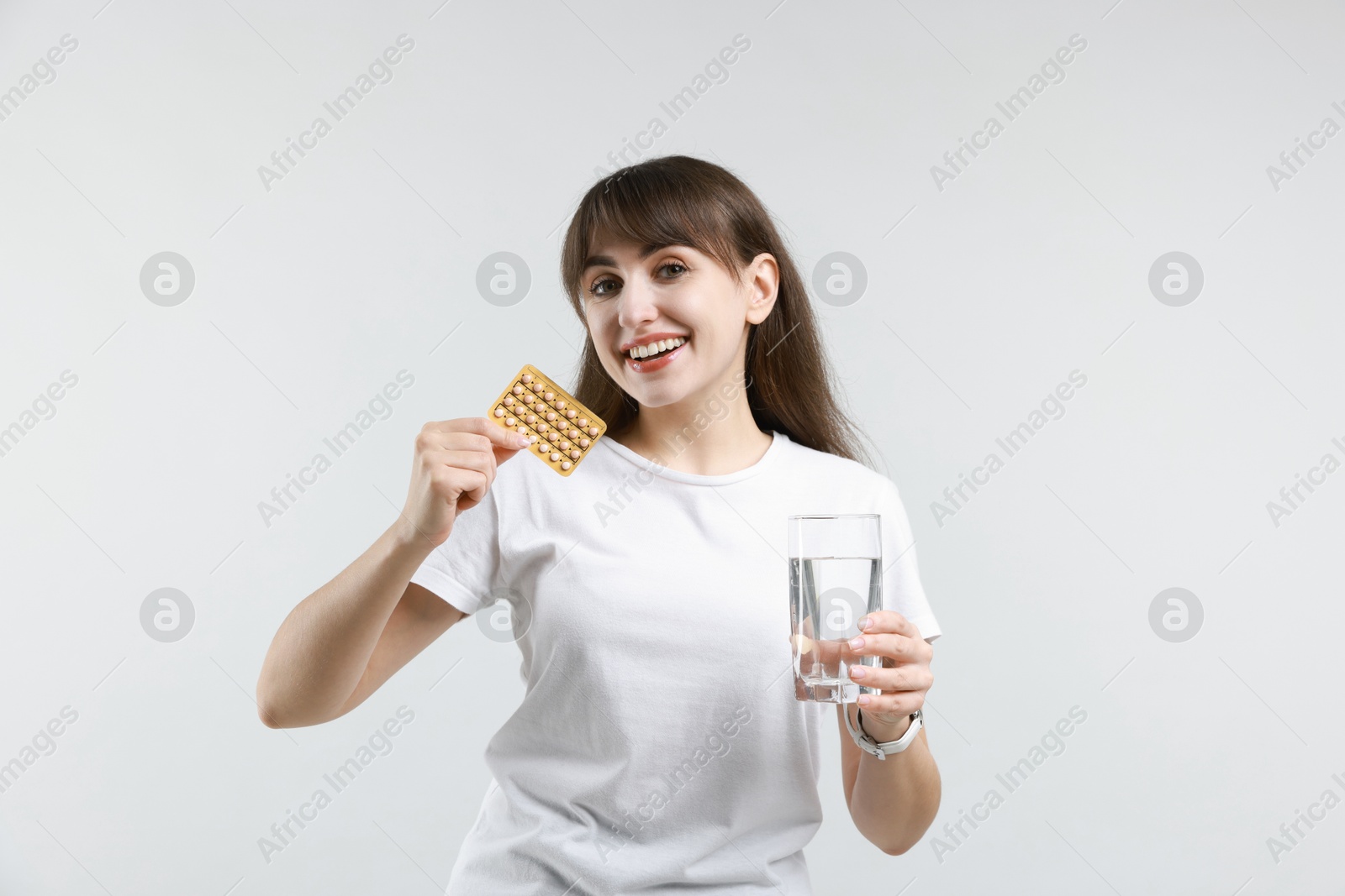 Photo of Smiling woman with contraceptive pills and glass of water on light background