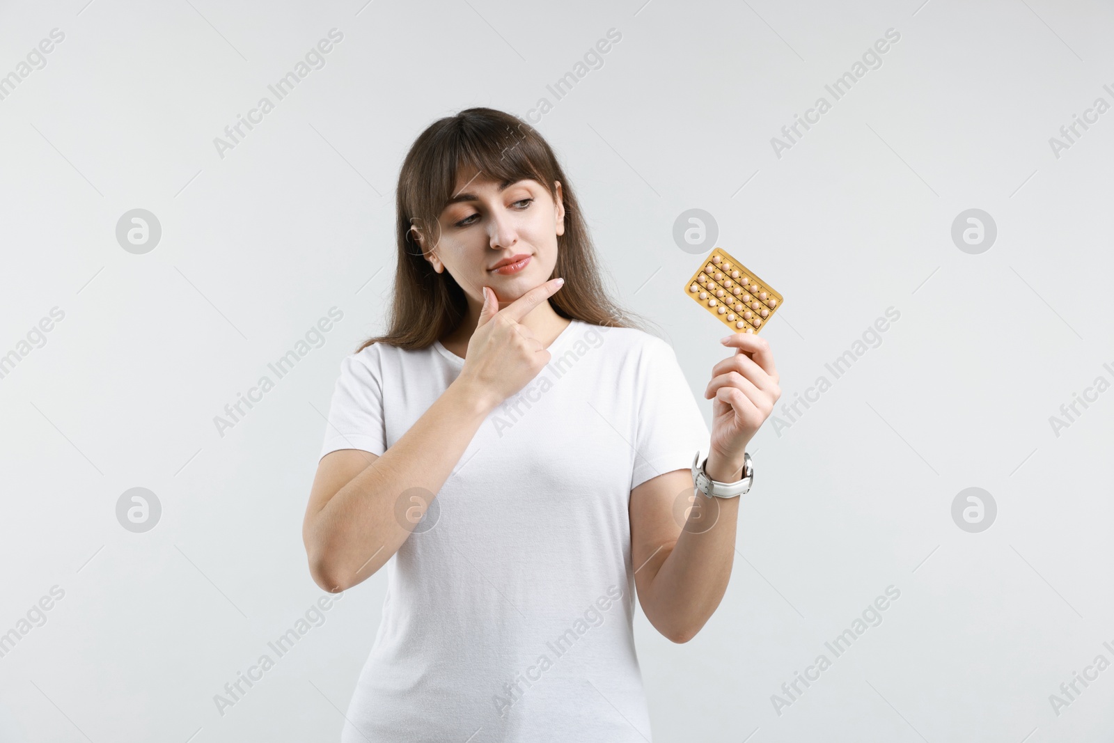 Photo of Young woman with blister of contraceptive pills on light background