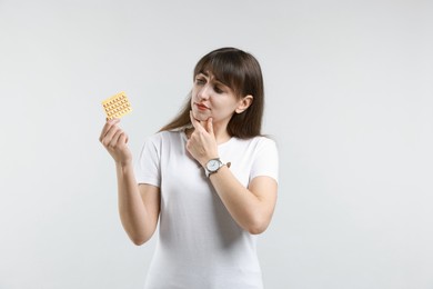 Photo of Young woman with blister of contraceptive pills on light background