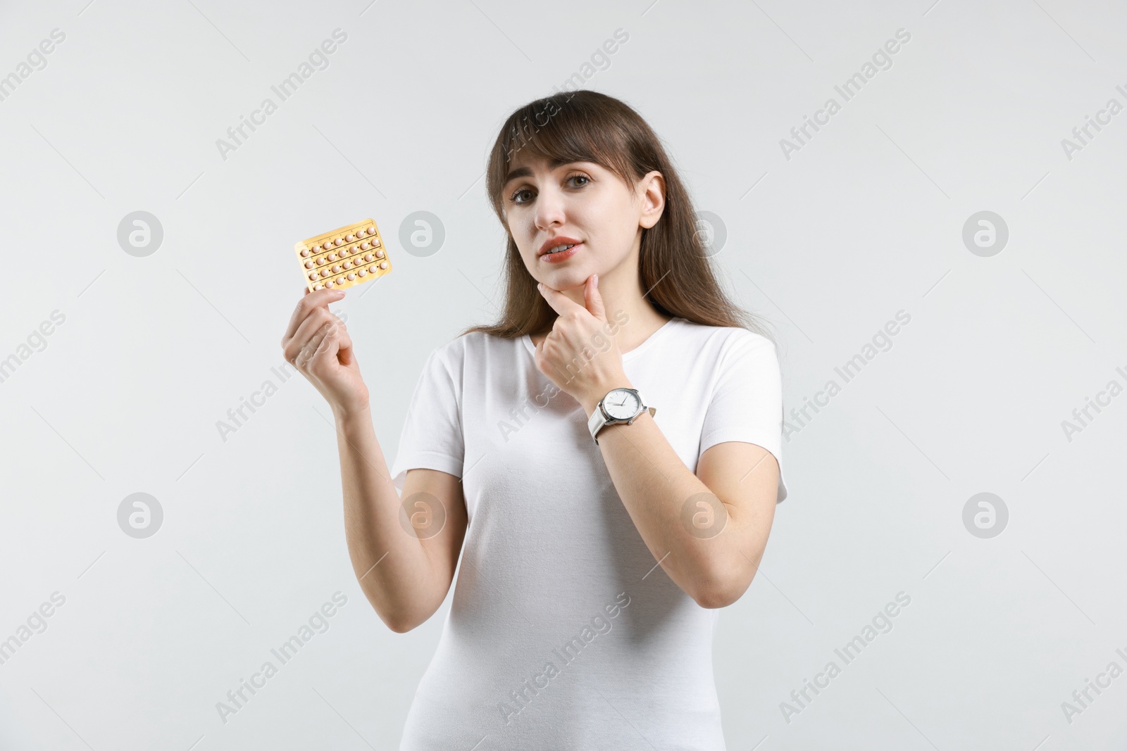 Photo of Young woman with blister of contraceptive pills on light background