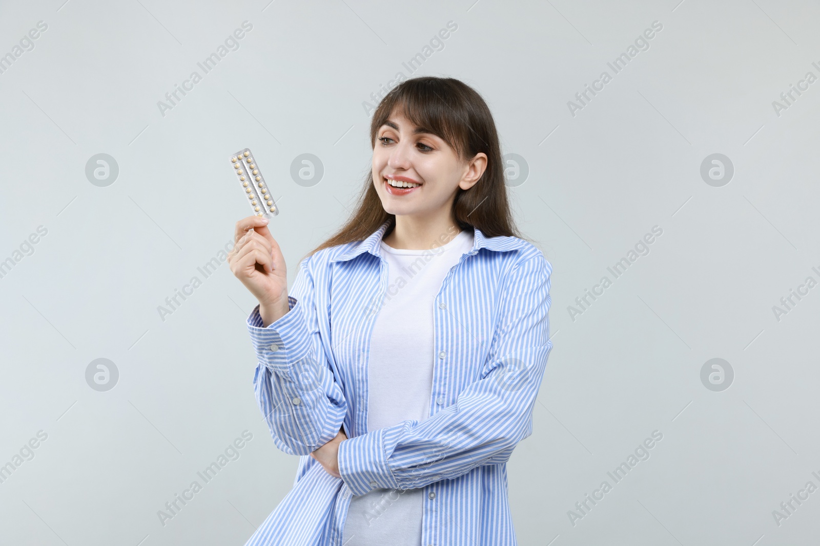 Photo of Young woman with blister of contraceptive pills on light background