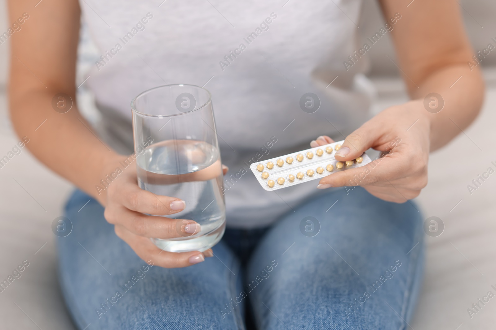 Photo of Woman with contraceptive pills and glass of water on sofa, closeup