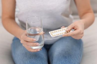 Photo of Woman with contraceptive pills and glass of water on sofa, closeup