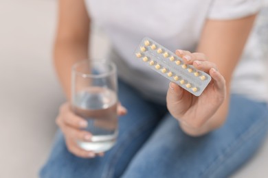 Photo of Woman with contraceptive pills and glass of water on sofa, closeup