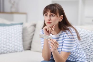 Photo of Upset woman with blister of contraceptive pills on sofa at home. Space for text