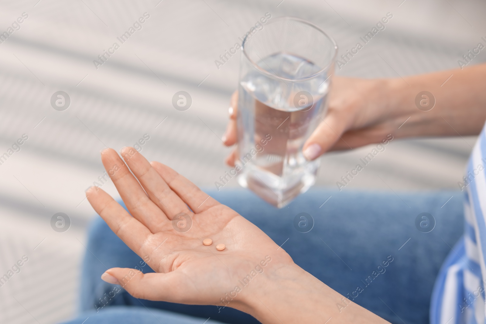 Photo of Woman with contraceptive pills and glass of water indoors, closeup