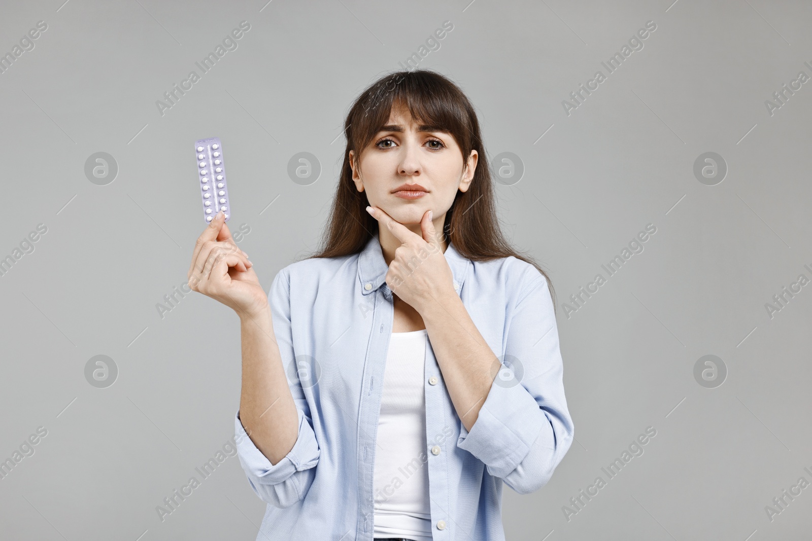 Photo of Pensive woman with blister of contraceptive pills on grey background