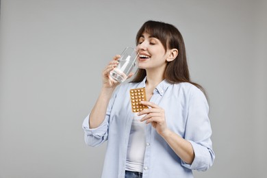 Photo of Young woman with contraceptive pills drinking water on grey background. Space for text