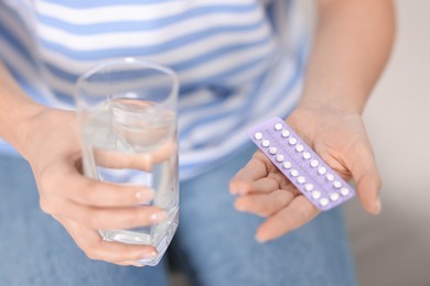 Photo of Woman with contraceptive pills and glass of water indoors, closeup