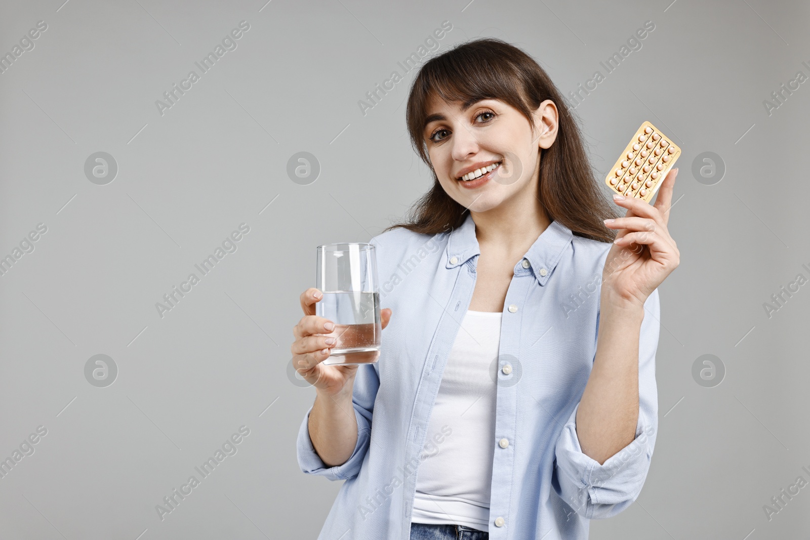 Photo of Smiling woman with contraceptive pills and glass of water on grey background. Space for text