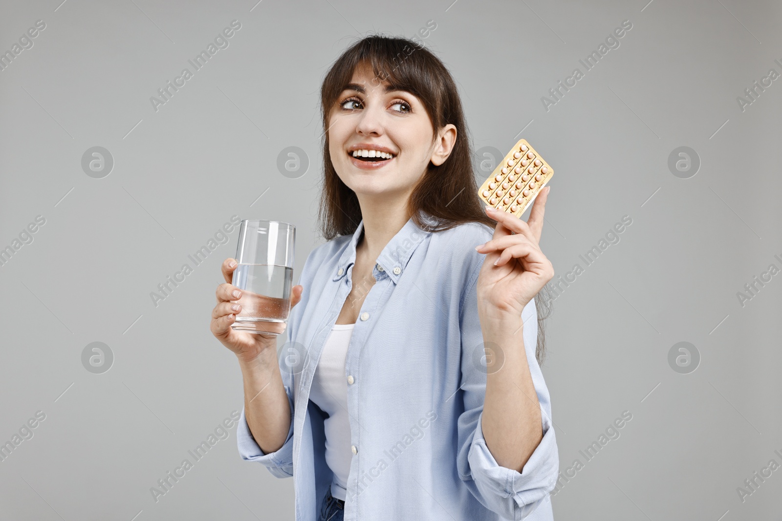 Photo of Smiling woman with contraceptive pills and glass of water on grey background