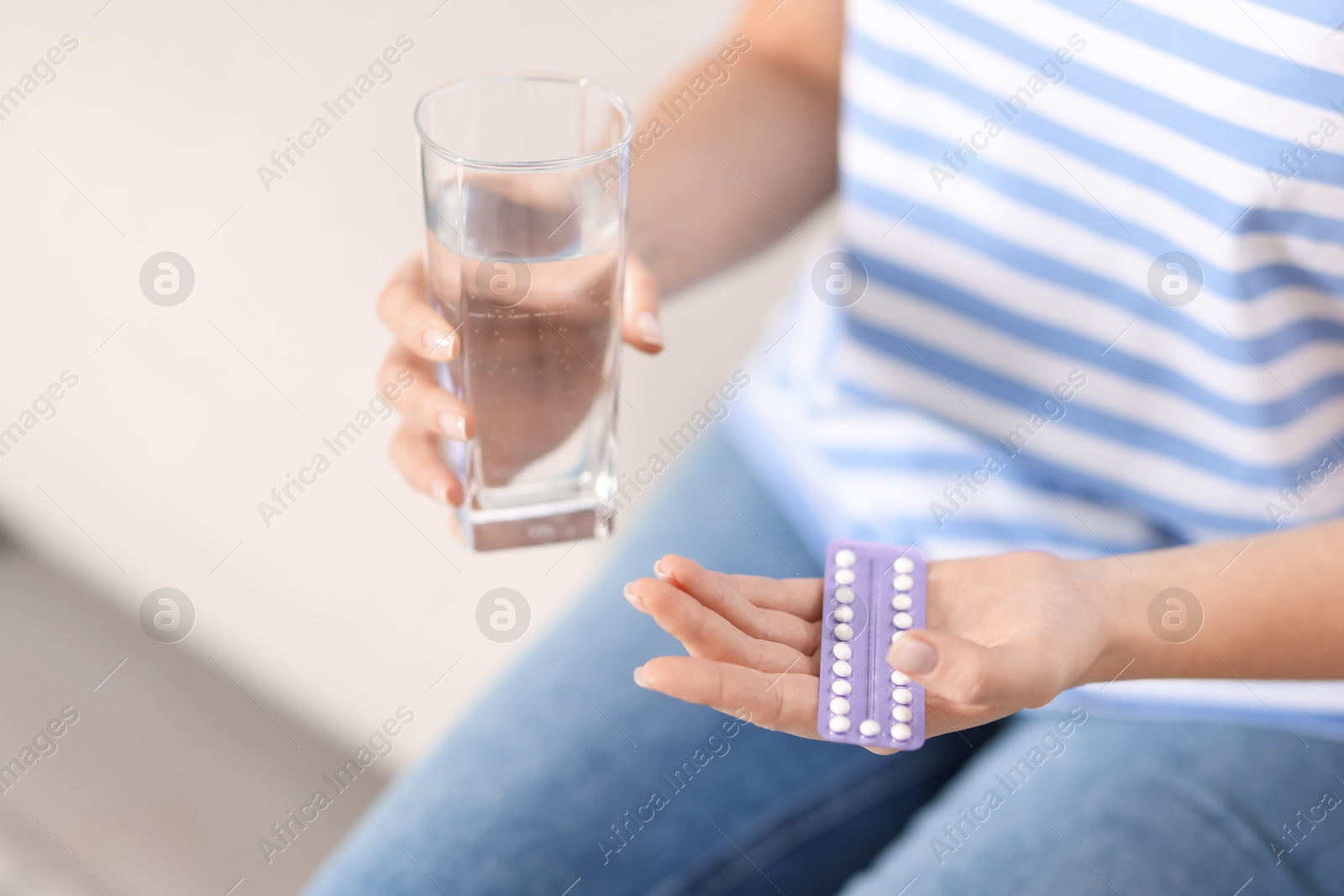 Photo of Woman with contraceptive pills and glass of water indoors, closeup