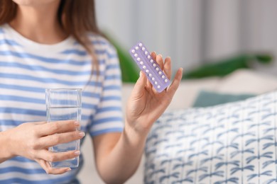 Photo of Woman with contraceptive pills and glass of water indoors, closeup. Space for text