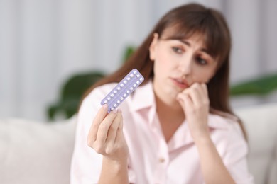 Photo of Upset woman with blister of contraceptive pills indoors, selective focus