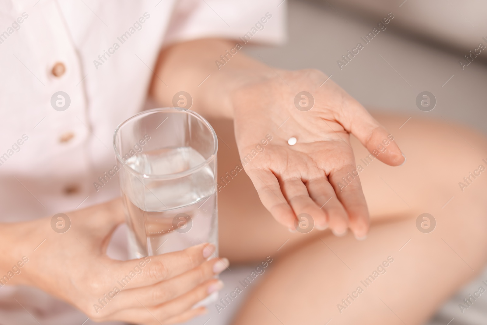 Photo of Woman with contraceptive pill and glass of water on bed, closeup