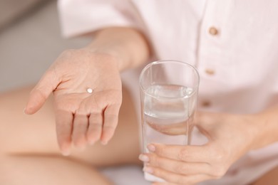 Photo of Woman with contraceptive pill and glass of water on bed, closeup