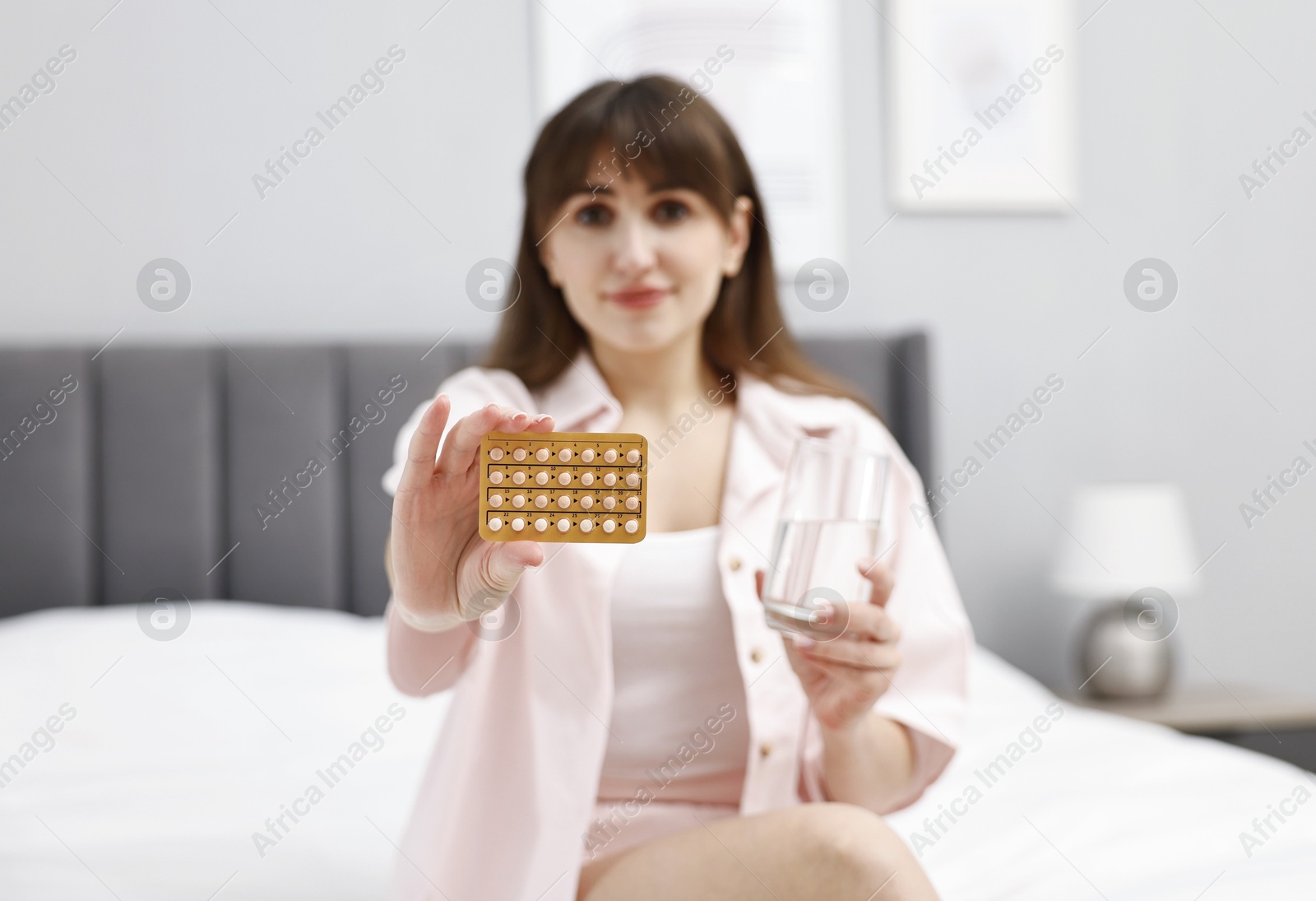 Photo of Woman with blister of contraceptive pills on bed at home, selective focus