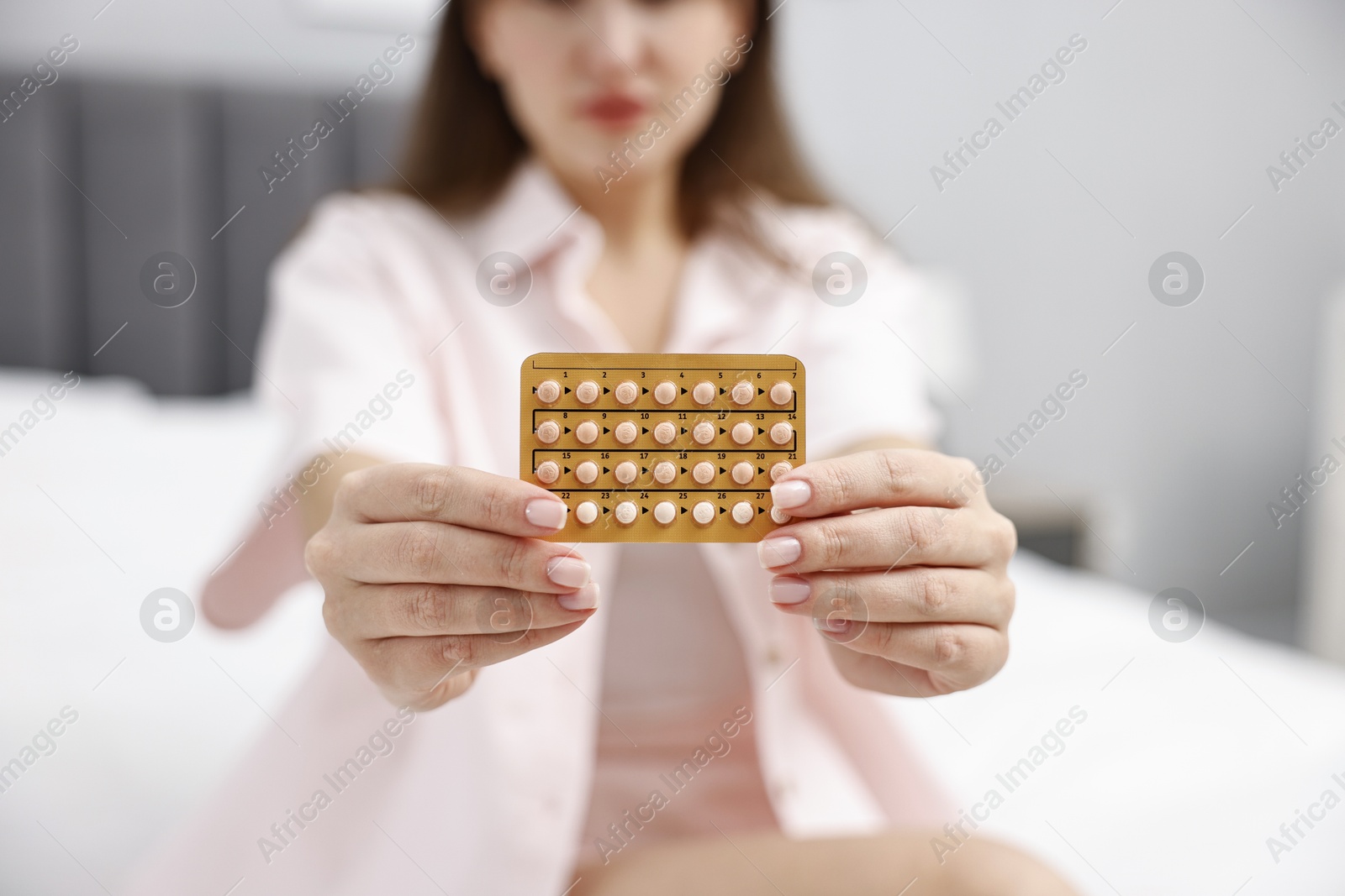 Photo of Woman with blister of contraceptive pills on bed indoors, closeup