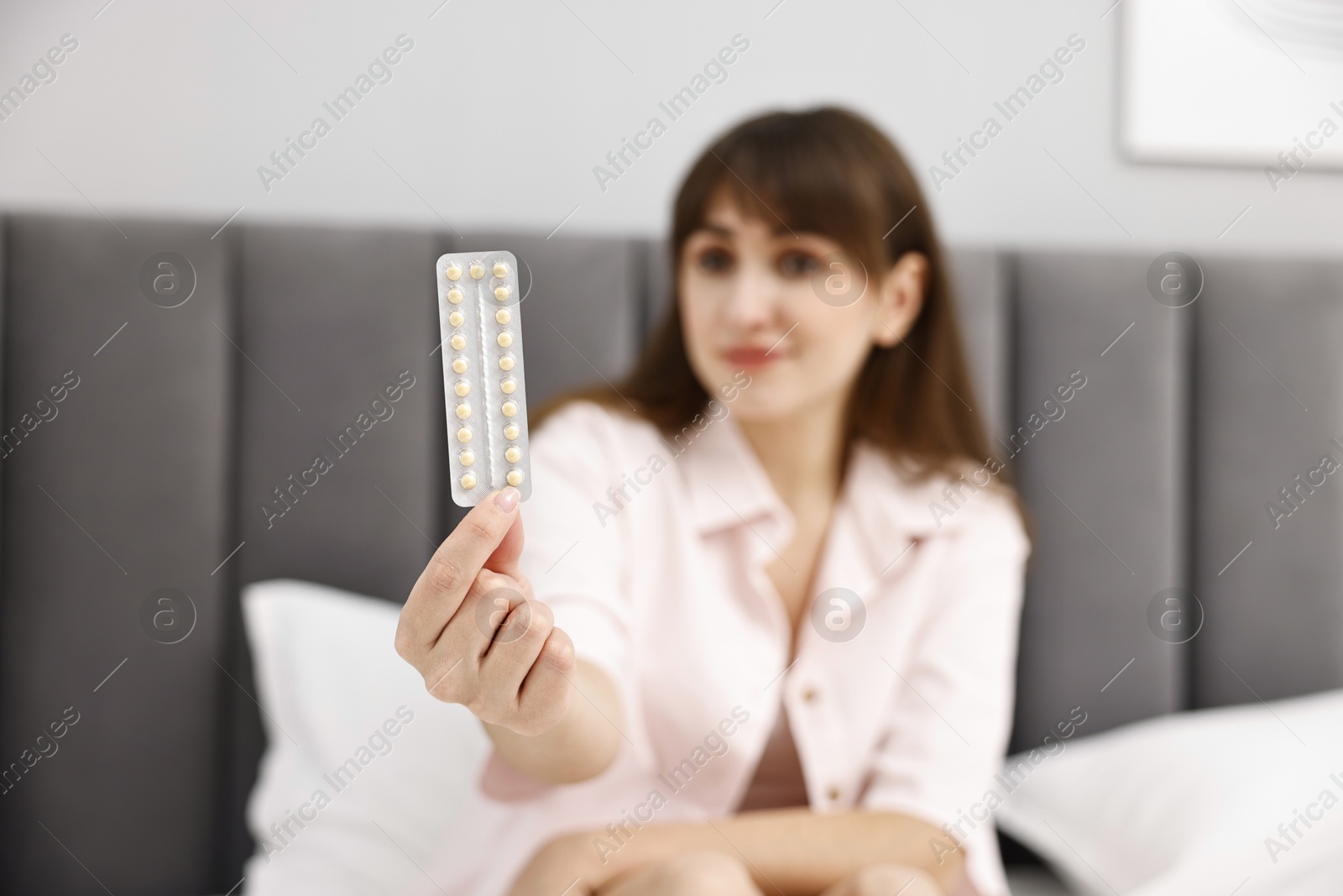 Photo of Woman with blister of contraceptive pills on bed indoors, selective focus