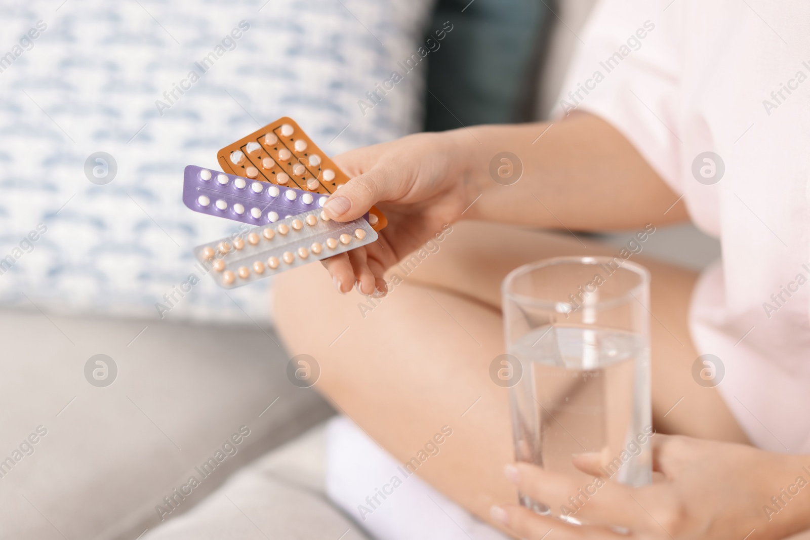 Photo of Woman with contraceptive pills and glass of water on sofa indoors, closeup