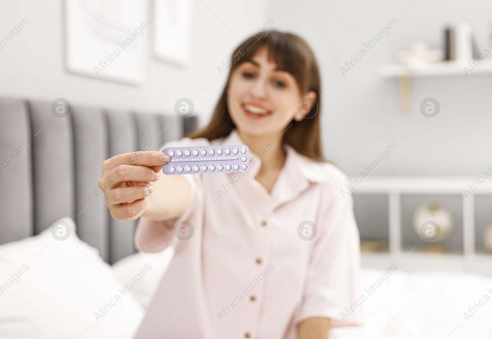 Photo of Woman with blister of contraceptive pills on bed indoors, selective focus