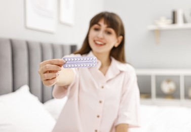 Woman with blister of contraceptive pills on bed indoors, selective focus